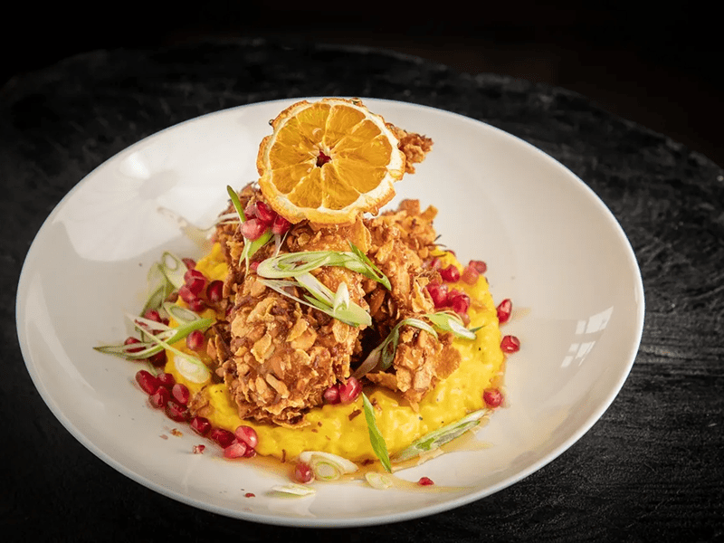 A vibrant plate of fried chicken with mango salsa and a dried orange garnish.