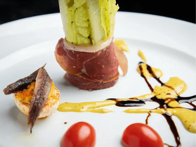 Gourmet dish with prosciutto, avocado, and artistic sauce presentation.