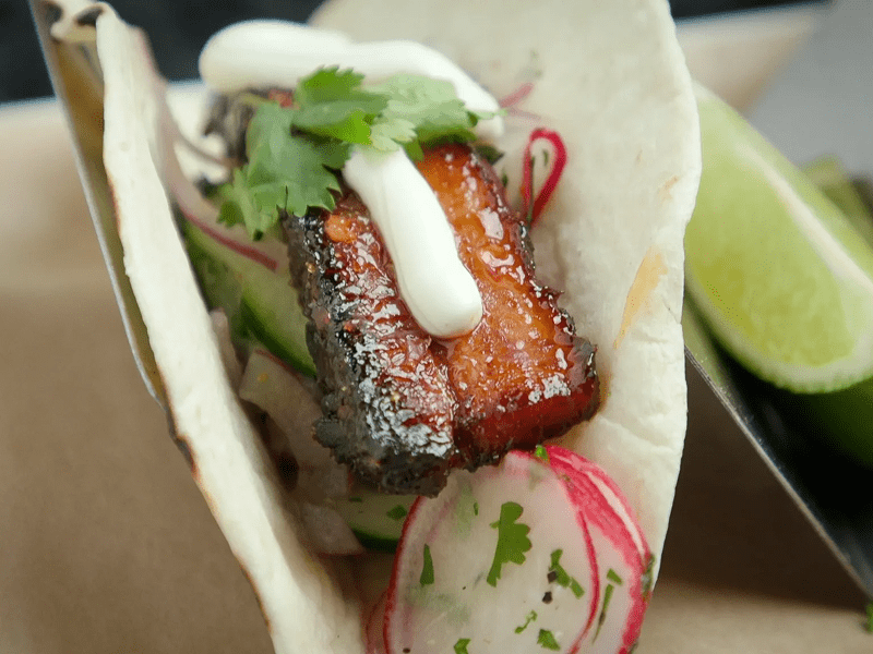 A taco with grilled meat, radish slices, and fresh herbs.
