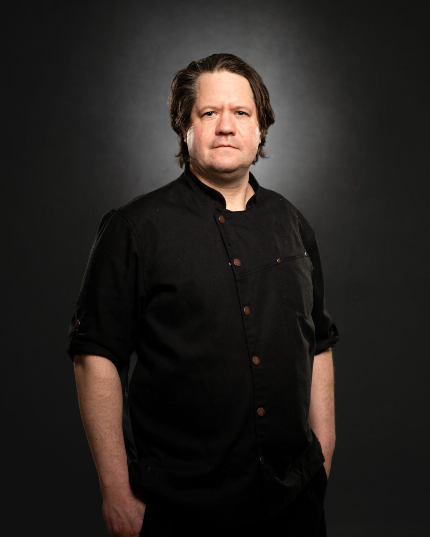 Portrait of a serious man in a black shirt against a dark background.