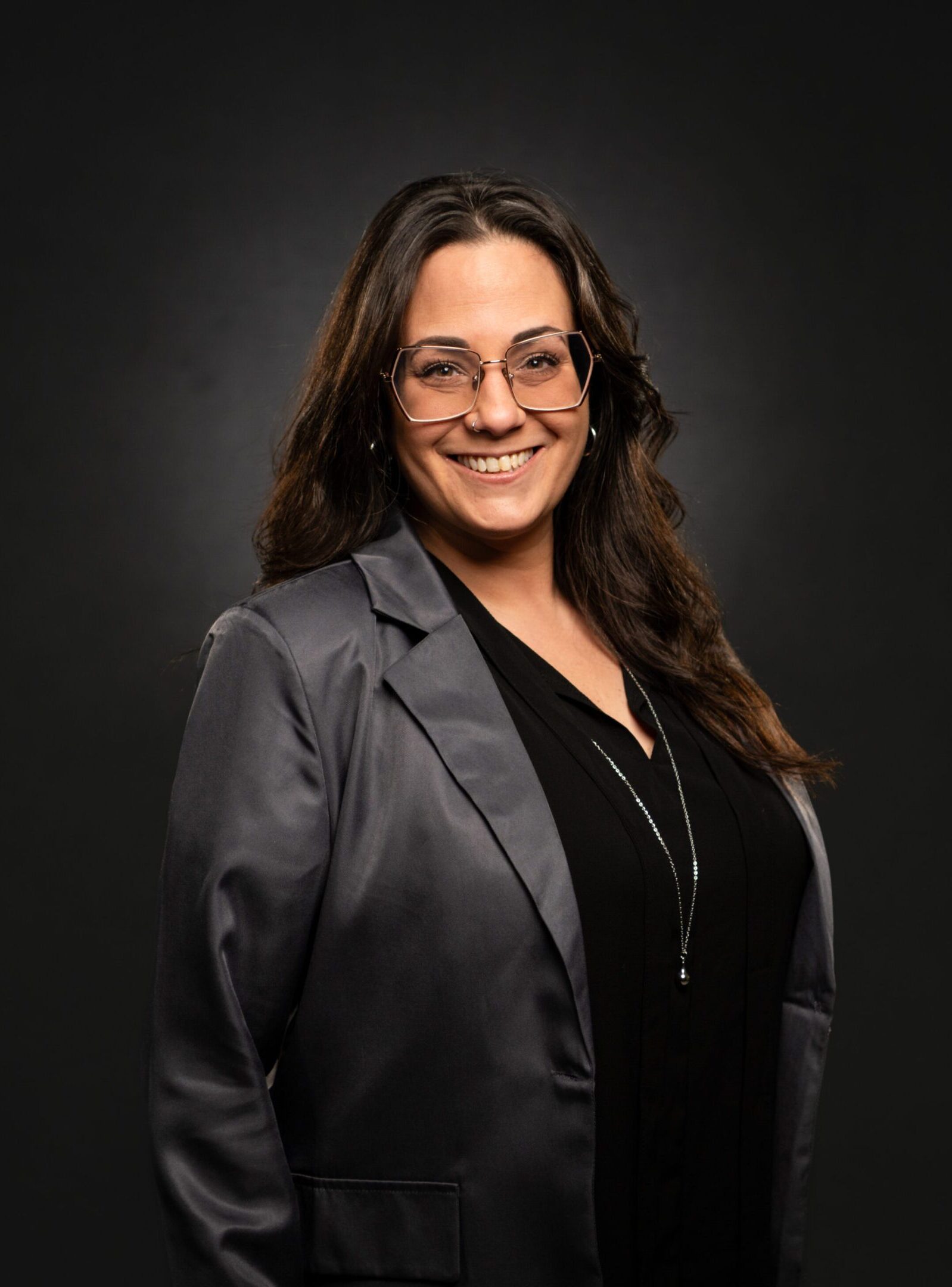 Professional woman smiling, wearing glasses and a blazer.