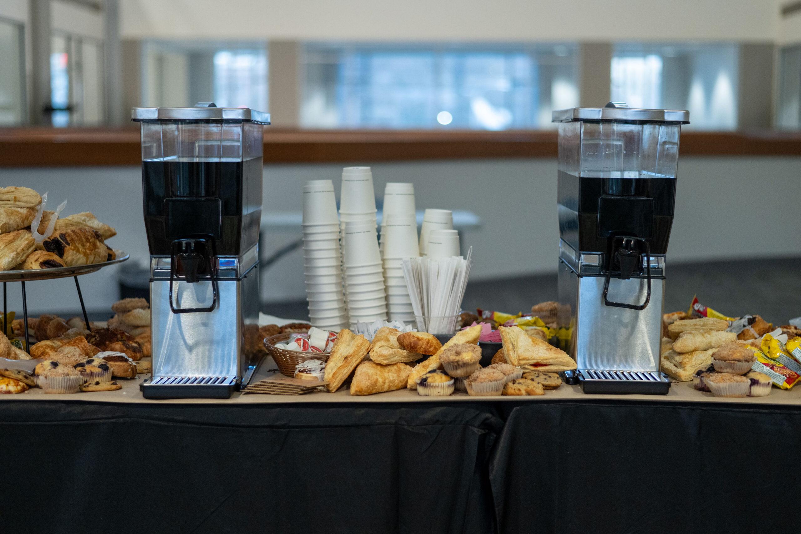 Coffee dispensers with pastries and cups on a table.