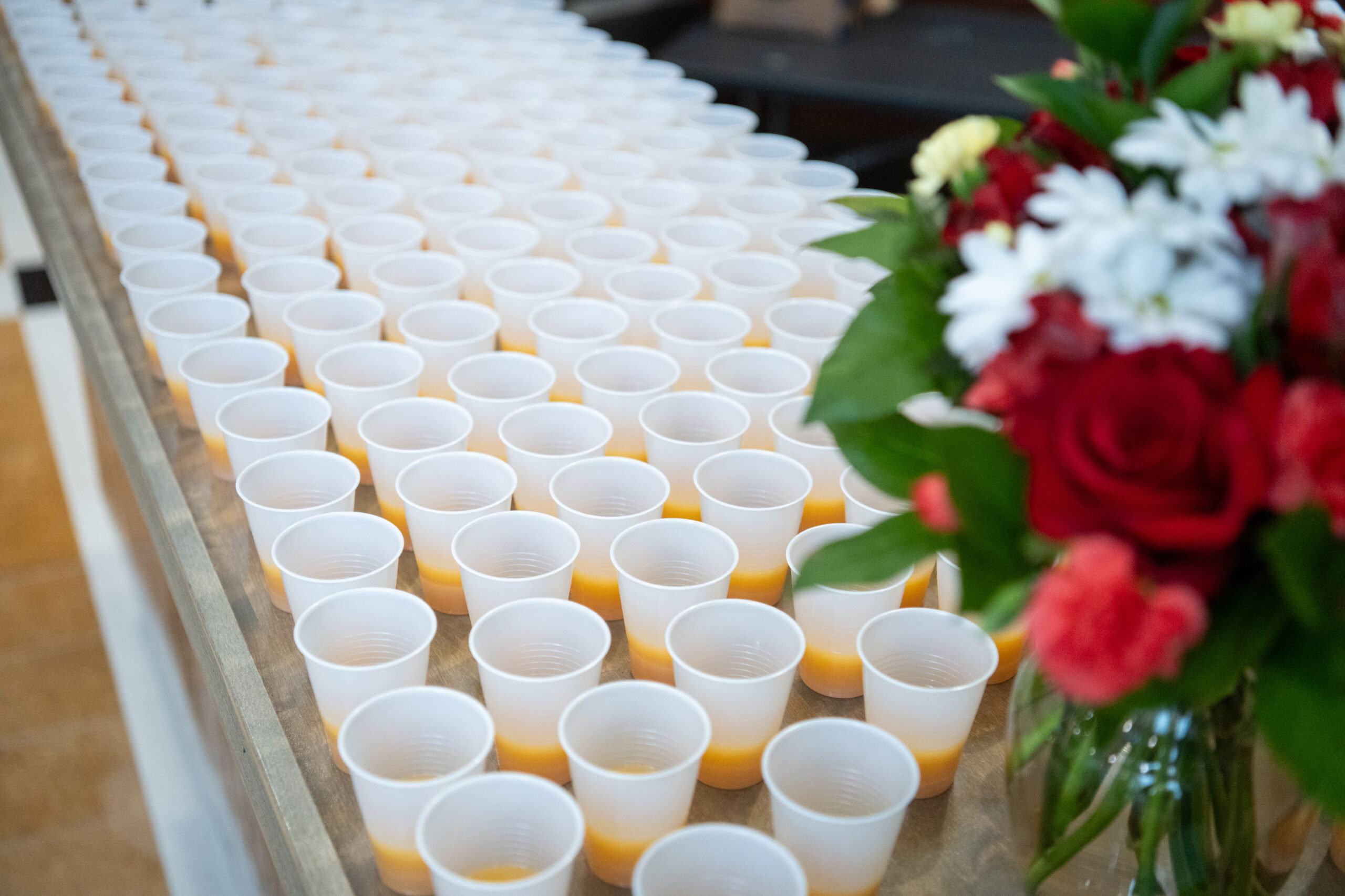 Rows of white cups filled with orange juice on a table.