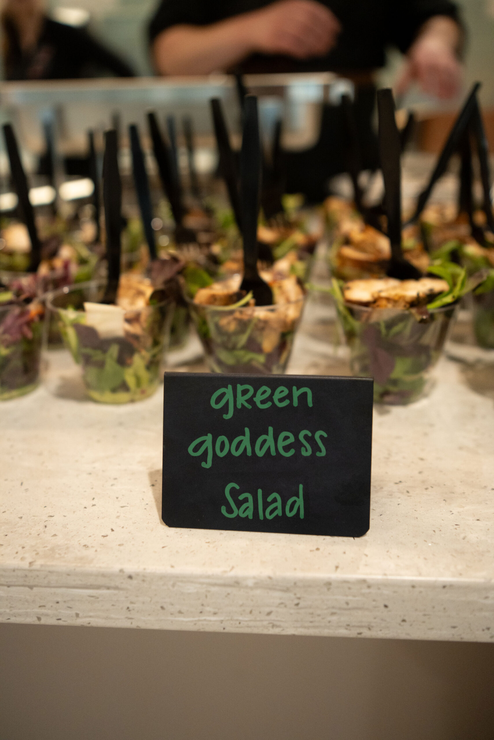 Small sign reading 'green goodness salad' in front of salad cups.