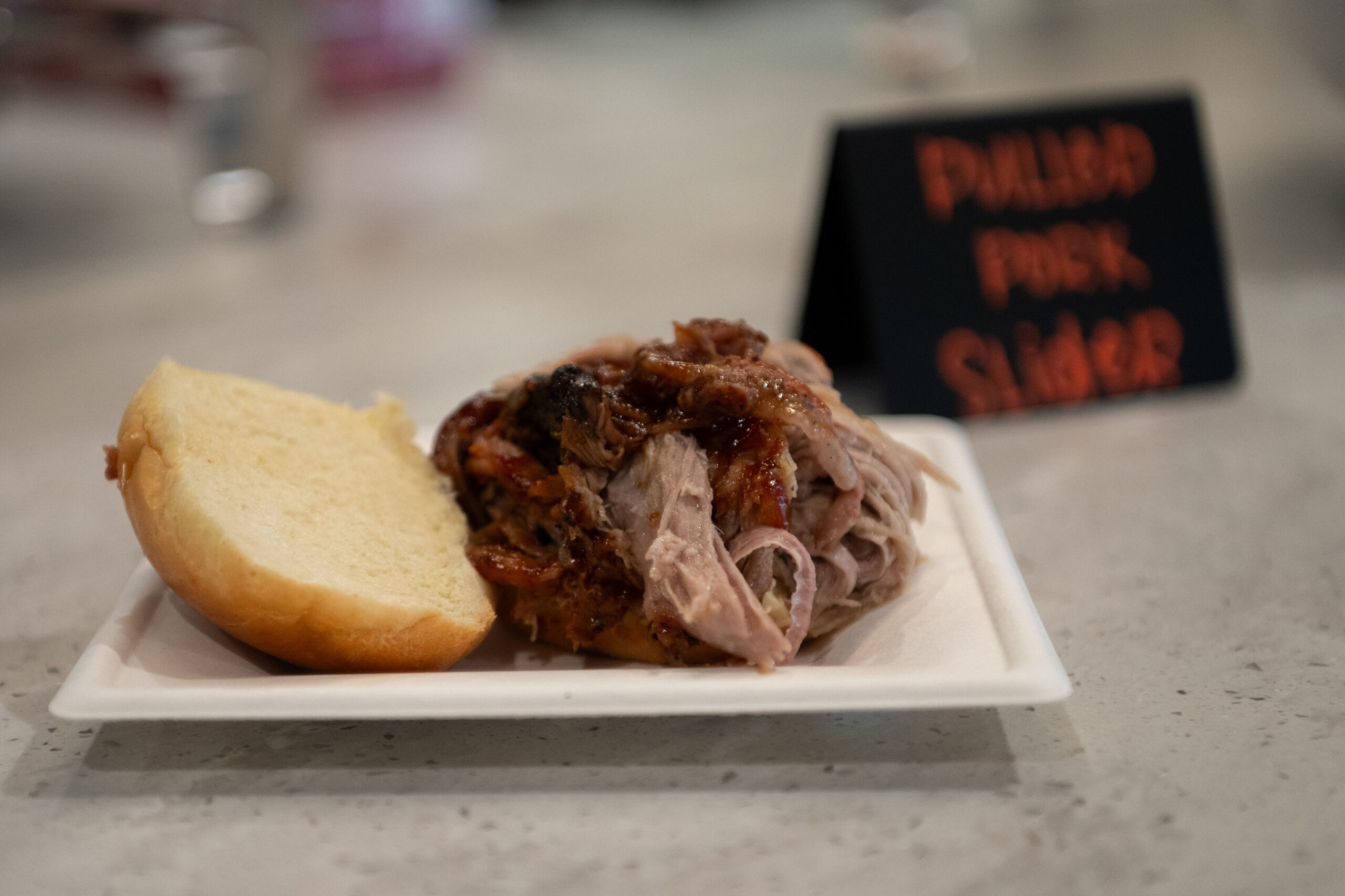 Pulled pork sandwich on a white tray with a bun.