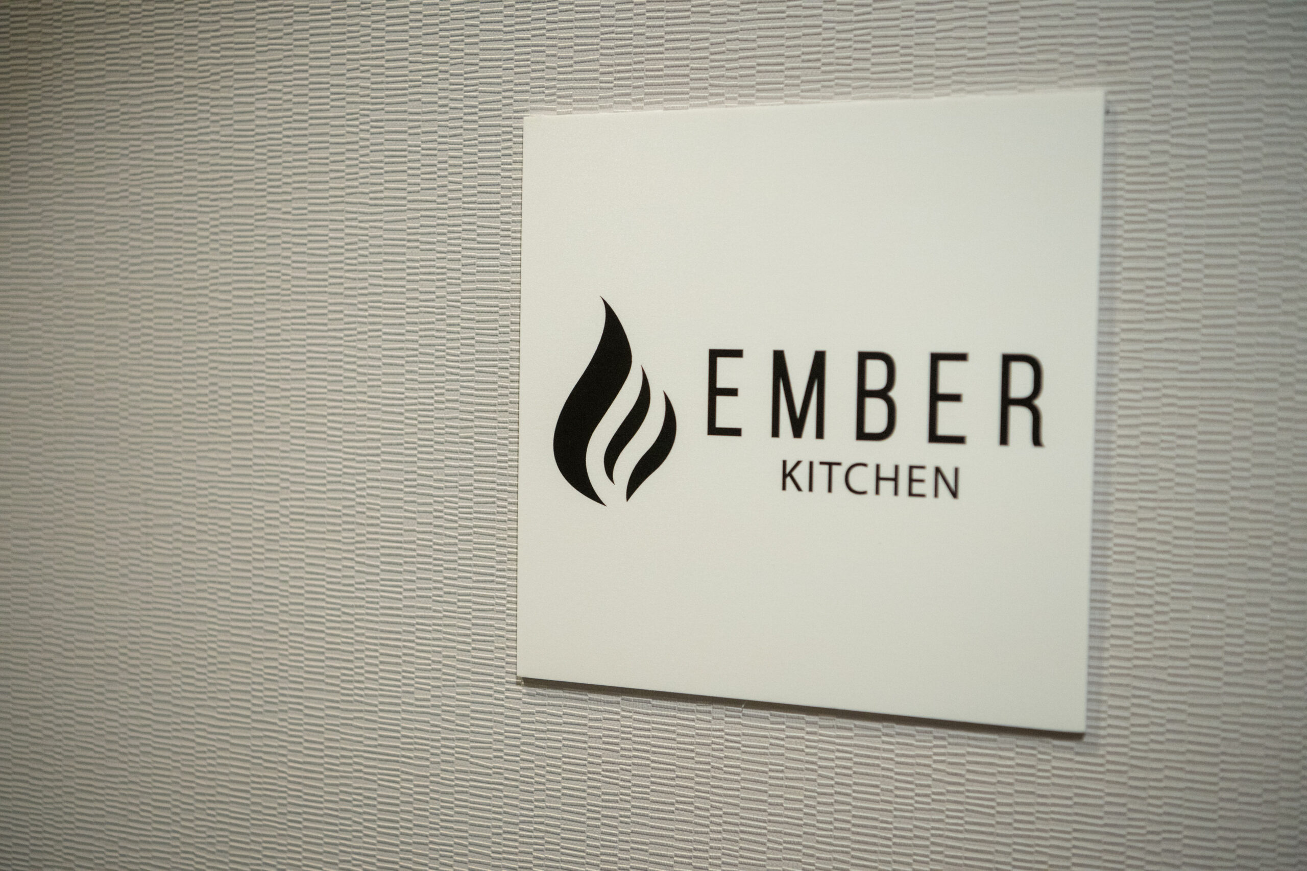 Sign for Ember Kitchen with a flame logo on a wall.