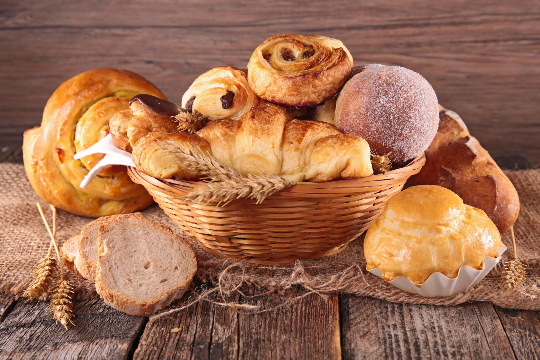 Basket of assorted fresh breads and pastries on a wooden table.