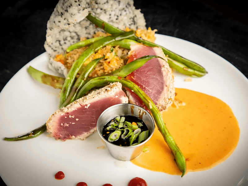 Seared tuna with asparagus, rice, and sauce on a black plate.