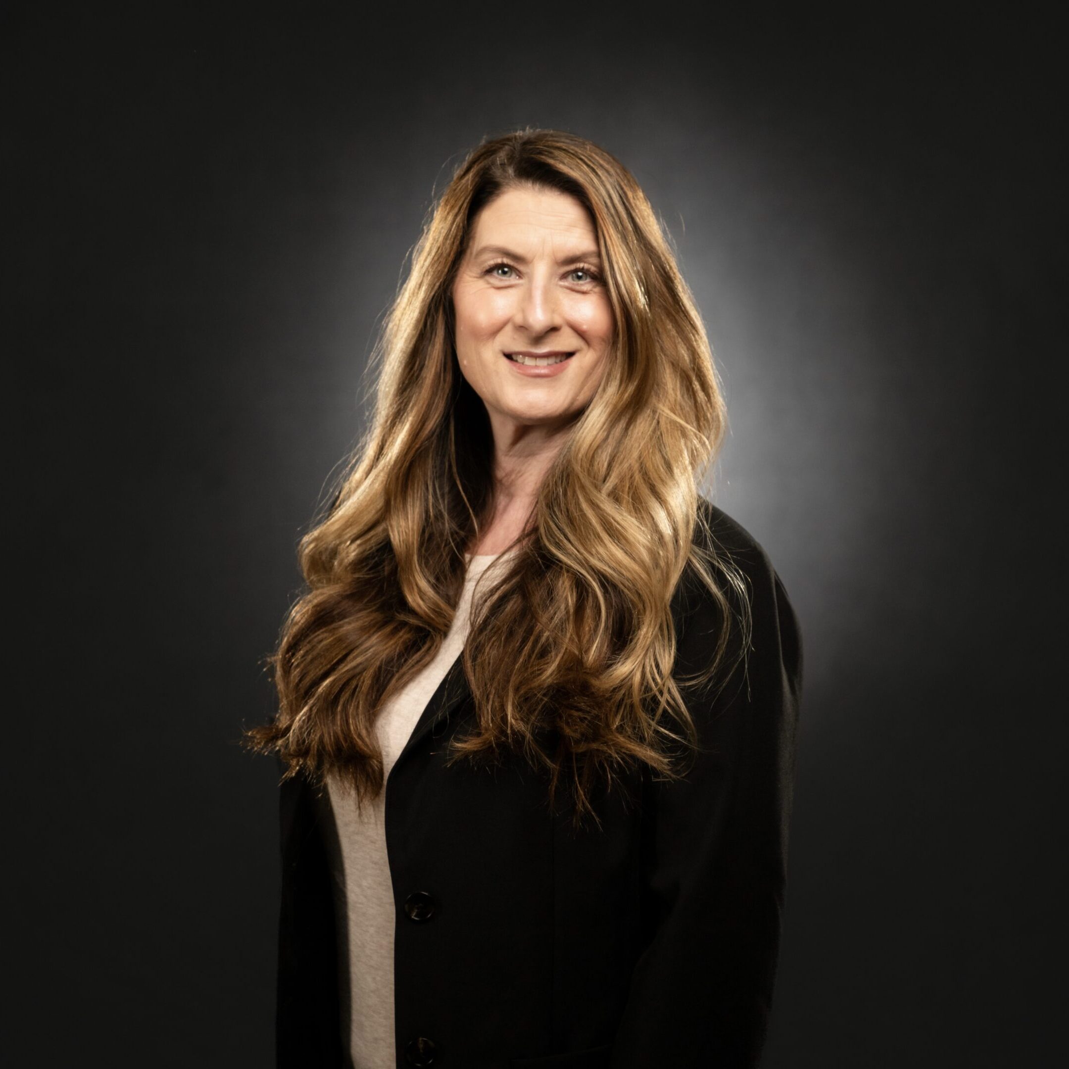 Professional woman with long hair in black attire against dark background.
